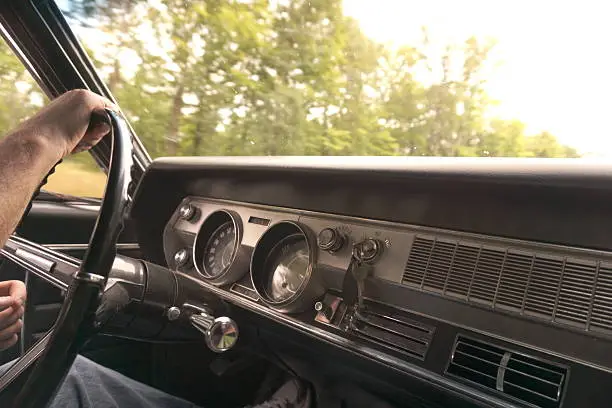 Interior dashboard and a hand on the steering wheel driving a 1967 Oldsmobile Cutlass Supreme Classic Collector's Car. Photographed on a Sony Alpha A5100 mirrorless camera.