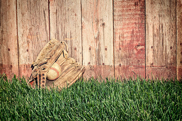 alte baseball handschuh und ball auf gras mit holz-zaun - baseball glove baseball baseballs old fashioned stock-fotos und bilder