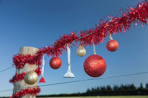 Christmas decorations of tinsel, baubles and dog whistles line a rural farm fence