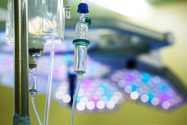 IV drip hanging on a pole in hospital Functioning IV drip hanging on a pole in hospital, with LED surgical lights in the background. Patient, illness, treatment, hospital, medicine and healthcare abstract and concept. chemotherapy drug stock pictures, royalty-free photos & images