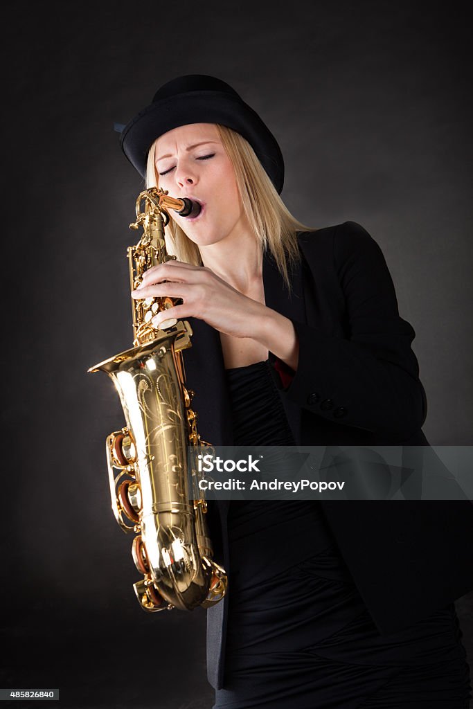 Beautiful young woman playing saxophone Beautiful young woman playing saxophone over black background 2015 Stock Photo