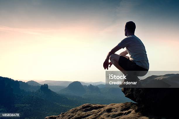 Young Man In Black Pants And Shirt Sit On Cliff Stock Photo - Download Image Now - 2015, Achievement, Activity
