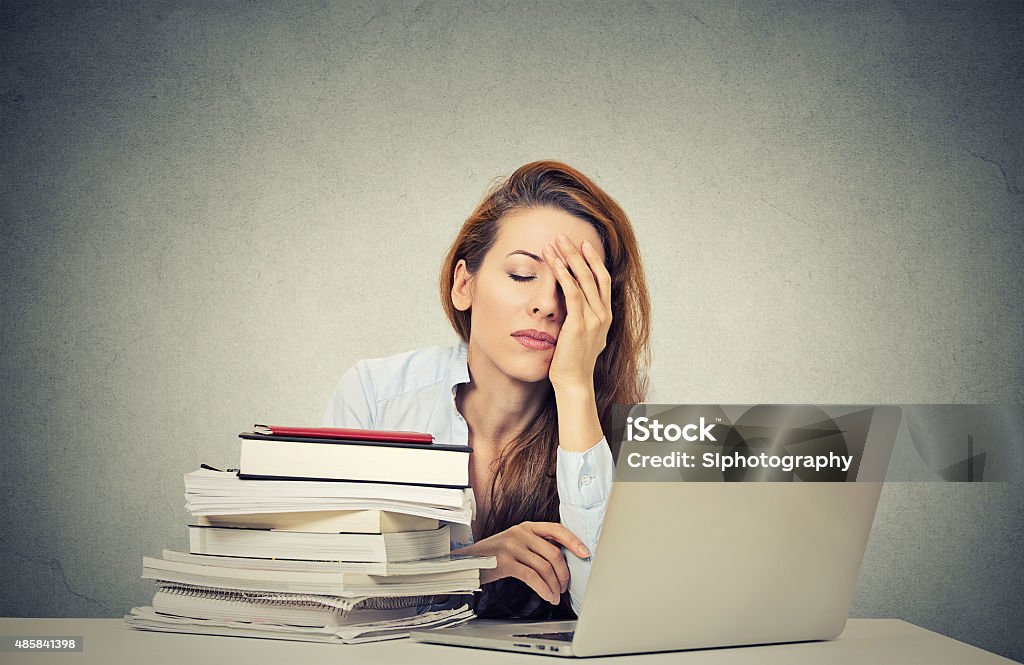 tired sleepy woman sitting at desk with books and computer Too much work tired sleepy young woman sitting at her desk with books in front of laptop computer isolated grey wall office background. Busy schedule in college, workplace, sleep deprivation concept Teacher Stock Photo