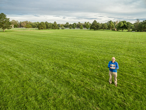 aerial shot of a male drone operator with a remote radio controller on a green grassy field