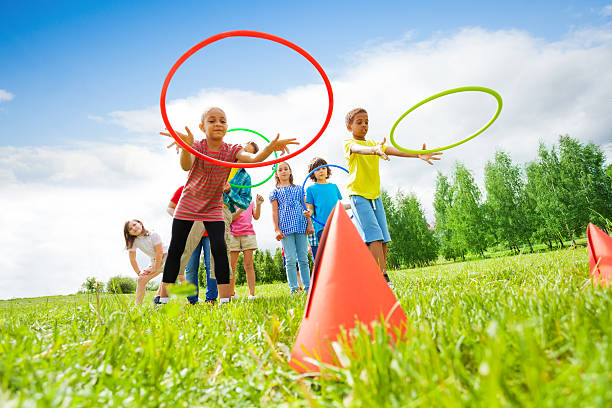 Kids throw colorful hoops on cones while competing Kids throwing colorful hoops on cones while competing with each other during summer sunny day relay stock pictures, royalty-free photos & images