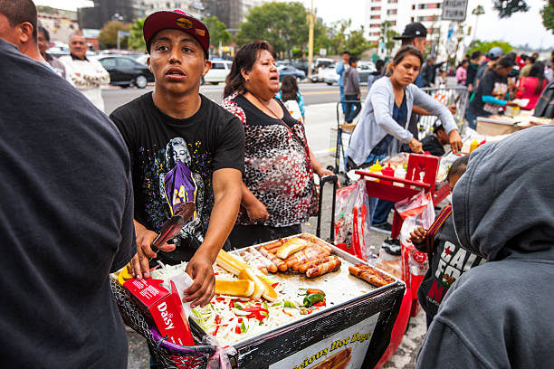 Los Angeles, USA - May 5, 2013: Young man cooking and selling Hot Dogs outdoors in Los Angeles downtown during Cinco De Mayo Celebration. Crowds of people buying fast food during celebrations