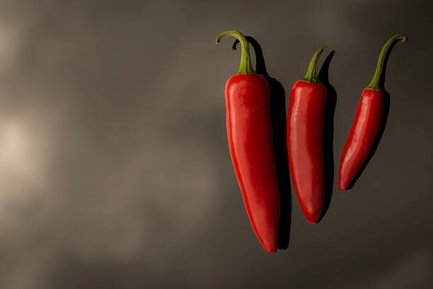 Three Chilli's to the right of a dark cloudy background stock photo