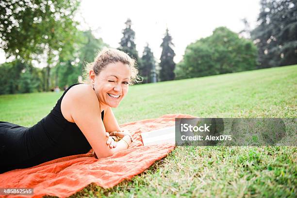 Mujer Leyendo Un Libro En El Parque Foto de stock y más banco de imágenes de Guiñar el ojo - Guiñar el ojo, Leer, Acostado