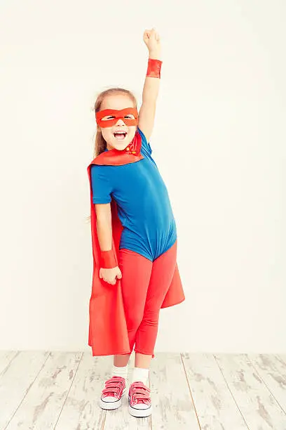 Funny little power super hero child (girl) in a blue raincoat. Superhero concept