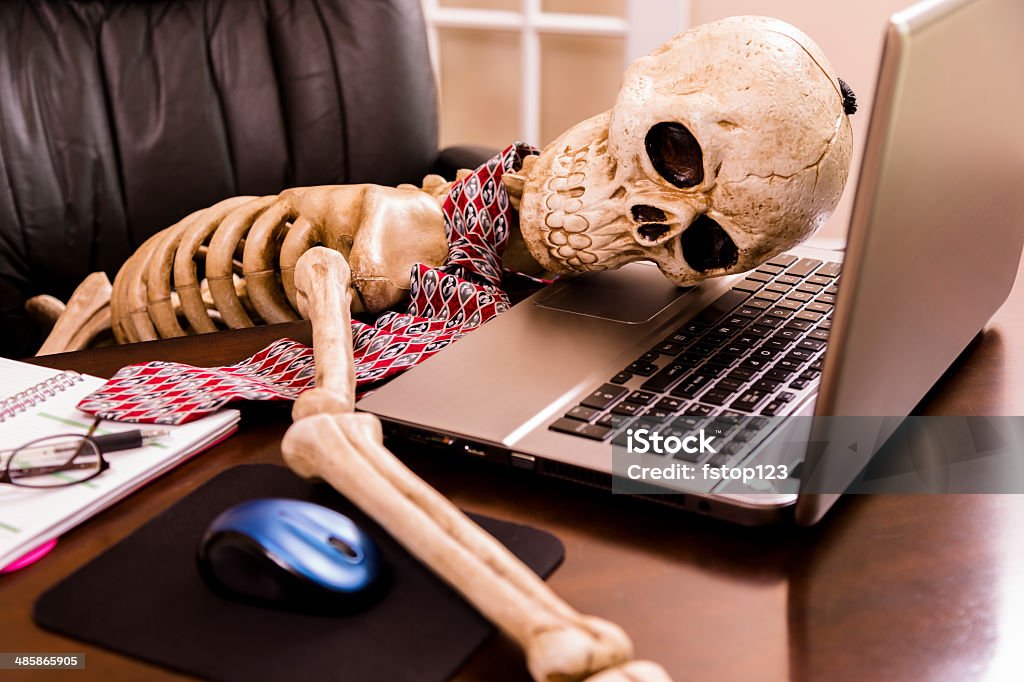 Working to death.  Business man's skeleton using laptop in office. Skeleton of a man with head on laptop in his office. This dedicated employee has worked himself to death!  Humor Stock Photo