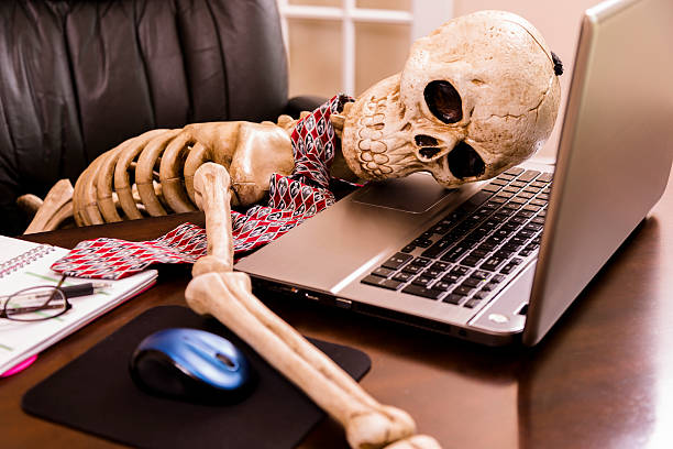 Working to death.  Business man's skeleton using laptop in office. Skeleton of a man with head on laptop in his office. This dedicated employee has worked himself to death!  patience photos stock pictures, royalty-free photos & images