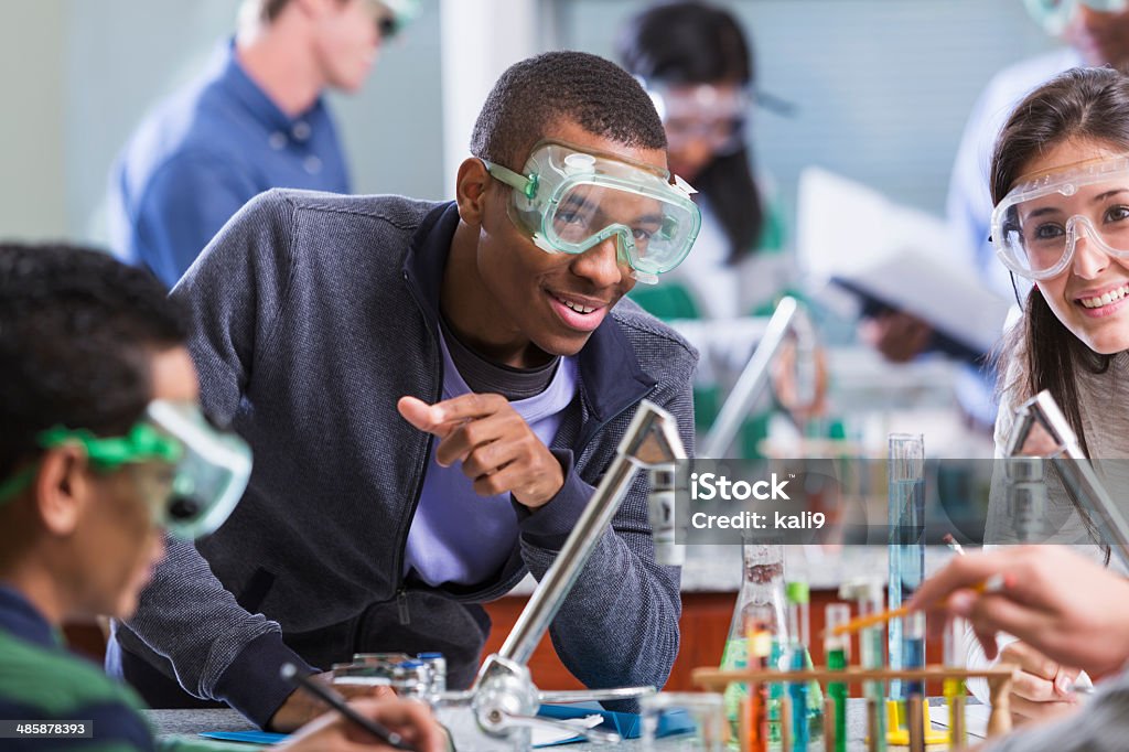 Multi racial students in chemistry class wearing safety glasses Multi-ethnic group of high school or college students in chemistry lab doing a science experiment.  Selective focus. Science Stock Photo