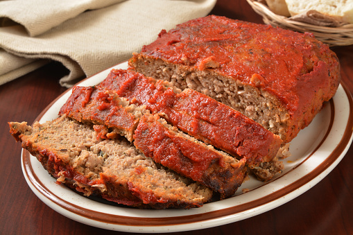 A serving platter with sliced meatloaf covered in tomato sauce