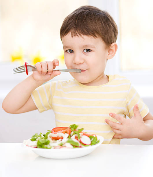 istock Cute little boy is eating vegetable salad 485883361