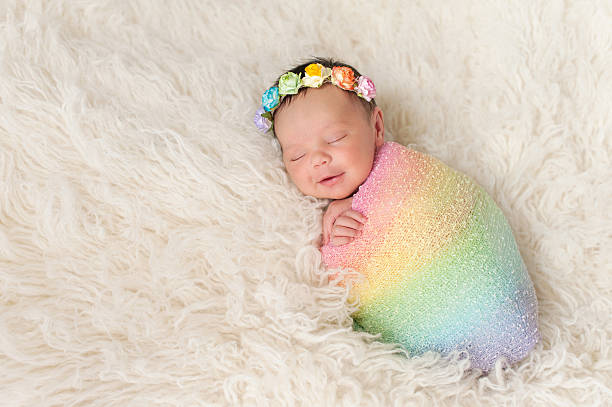 Smiling Newborn Baby Girl Wearing a Rainbow Colored Swaddle A smiling nine day old newborn baby girl bundled up in a rainbow colored swaddle. She is lying on a cream colored flokati (sheepskin) rug and wearing a crown made of roses. bundle photos stock pictures, royalty-free photos & images