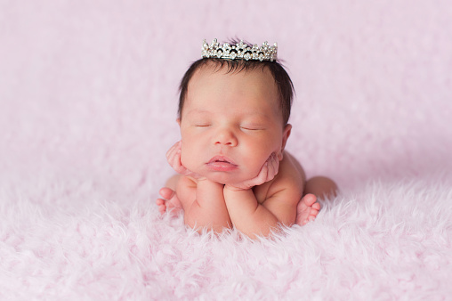 Portrait of nine day old sleeping newborn baby girl. She is wearing a dainty rhinestone crown and is posed with her chin in her hands.