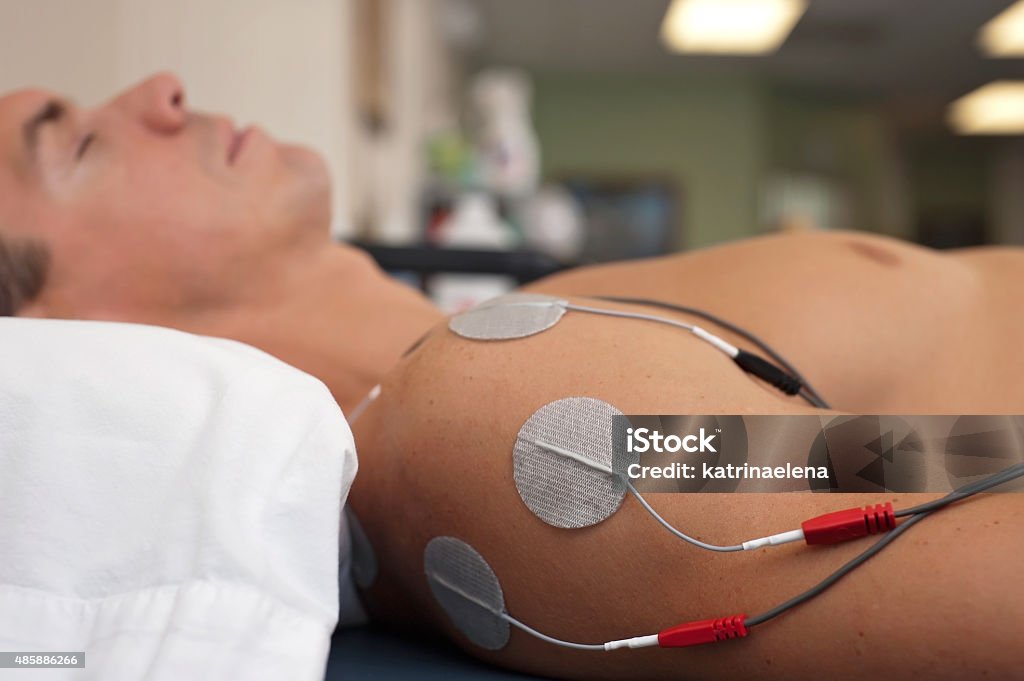 Shoulder Electrical Stimulation / TENS Physical therapy or chiropractic treatment of a male patient's injured shoulder using transcutaneous interferential electrical stimulation (TENS) for pain management. 2015 Stock Photo