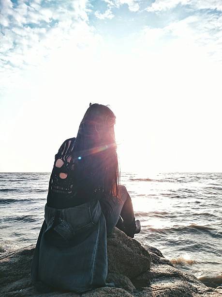 The Back of a Girl sitting on a Rock in Front of the Sea