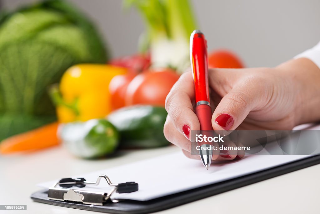 Nutritionist's desk Nutritionist writing medical records and prescriptions with fresh vegetables Nutritionist Stock Photo
