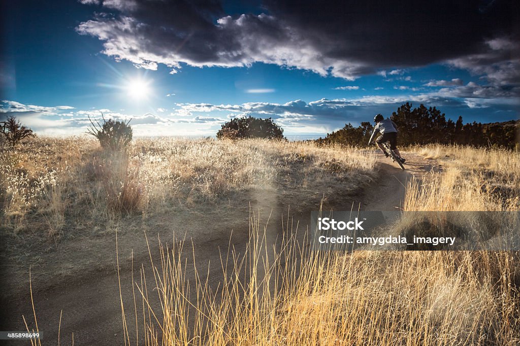 mountain biking! a mountain biker leans hard and fast into a turn through a desert landscape with a dramatic sky of sunshine and clouds stands above.  horizontal wide angle composition.   Albuquerque - New Mexico Stock Photo