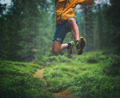 A man exercise trail running in a green and wet forest, jumping over tree roots.