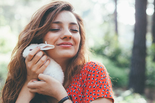 Beautiful and cute young woman holding a little white bunny and looking at camera posing at forest