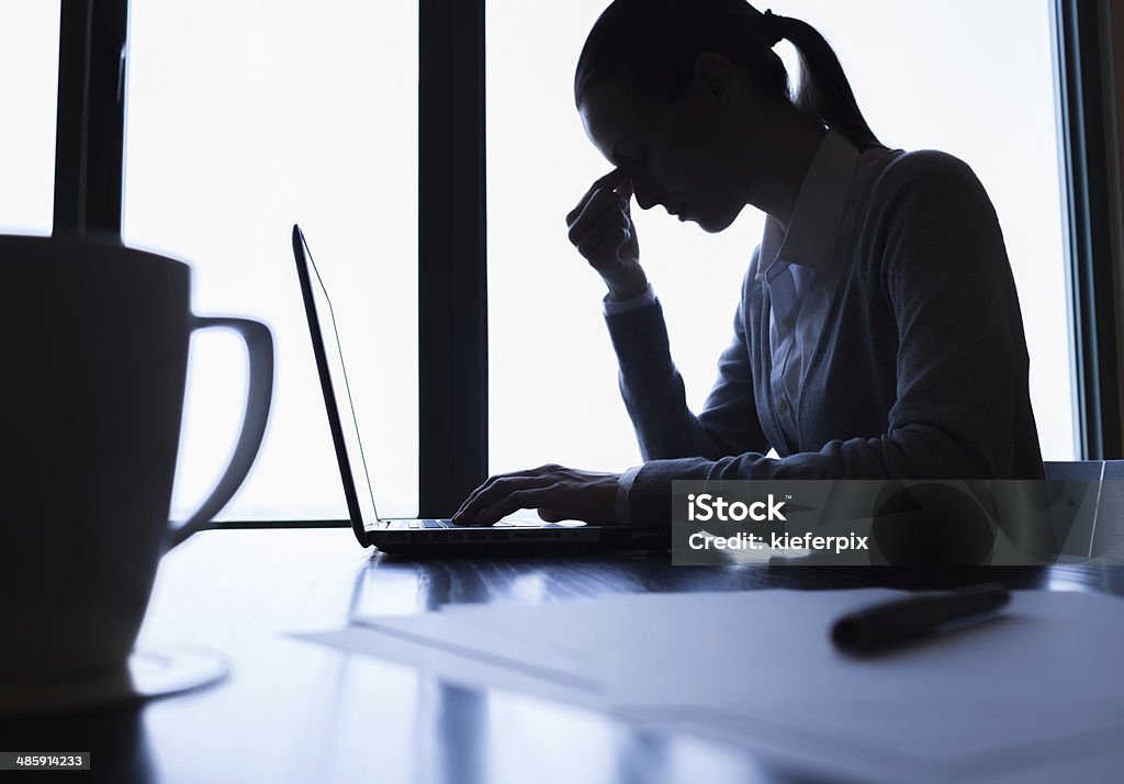 Stressed business woman Silhouette of stressed business woman in the office. Desk Stock Photo