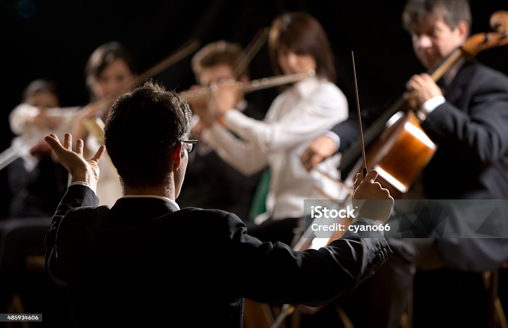 Conductor directing symphony orchestra Conductor directing symphony orchestra with performers on background. Musical Conductor Stock Photo
