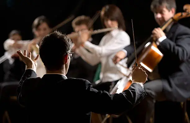 Conductor directing symphony orchestra with performers on background.