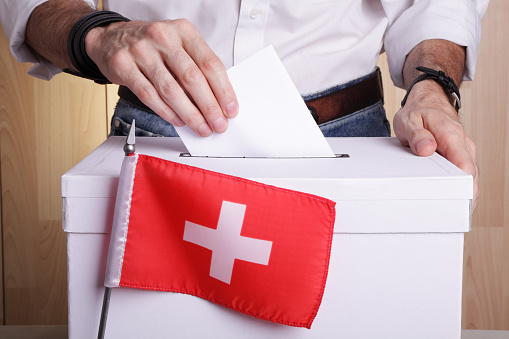 Unrecognizable citizen casting his vote. The Swiss flag is in front of the polling box with