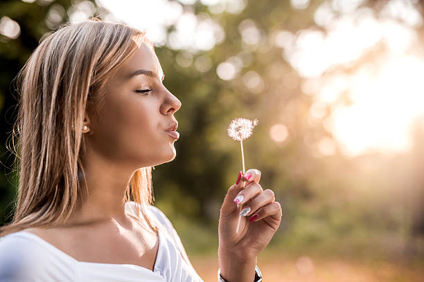 istock Young beautiful woman blowing dandelion at sunset. 485938950