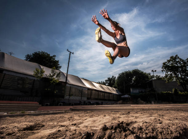 Low angle view of young athletic woman in long jump. Below view of a young female athlete in a long jump. long jump stock pictures, royalty-free photos & images