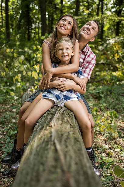 Beautiful young family sitting on fallen tree in the forest and enjoying.