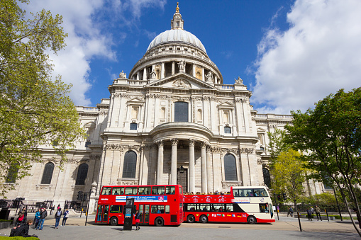 London, England - April 18, 2014: Locals and tourists walk outside St Paul's Cathedral in London. In the background are typical London double decker red buses