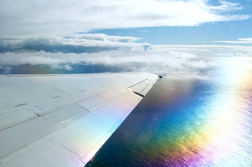 Wing of airplane flying above clouds in the sky and with a view of the ocean in background