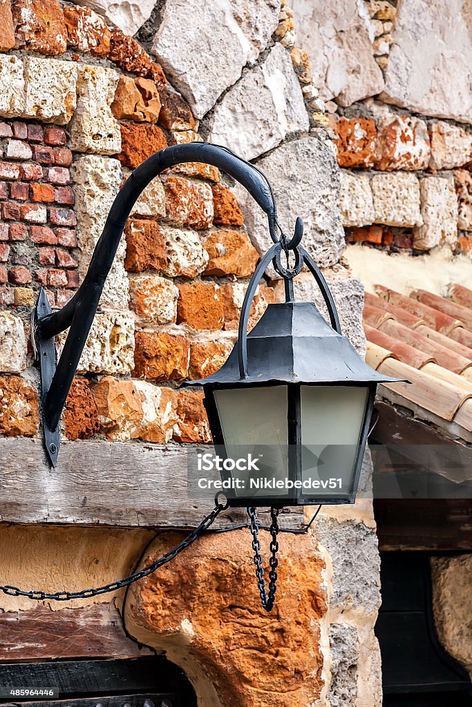 The old lantern hanging on a brick wall background. The old lantern hanging on a brick wall background. Forged black lantern on a background of the old wall of red brick. Clear day. 2015 Stock Photo