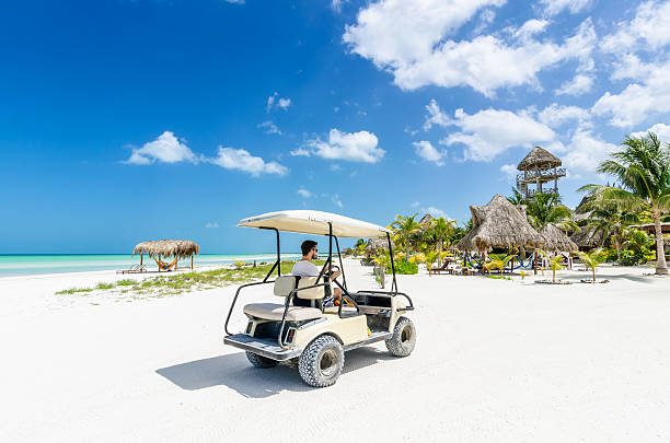 Young man driving golf cart along tropical sandy beach