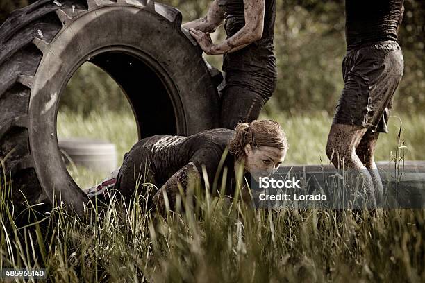 Group Of Friends Doing Tyre Obstacle During Mud Run Stock Photo - Download Image Now