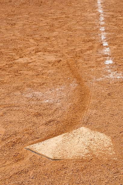 Home plate on a small town baseball field after a ball game.  The baseball field is full of foot prints and even a bicycle tire track across home plate  Children's footprints as still present in the sandy infield.  Children's playground.