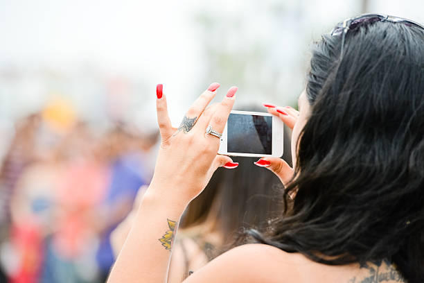 Venice Beach, USA - May 12, 2013: Woman photographing with iPhone in crowd of people watching entertaining show on the beach. 