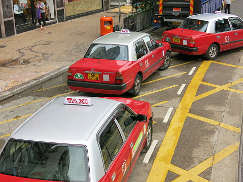 Hong Kong, China - August 14, 2015: A street of taxis with other cars on the road in Hong Kong. Pedestrians walks on the sidewalk. 