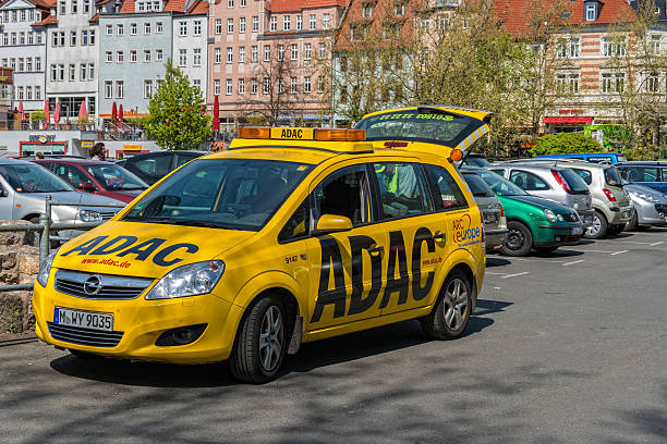 ADAC car helps at a parking place Jena, Germany - April 17, 2014: Service car of automobile club ADAC Germany is standing in a parking area and the man helps a user of a car with his problems. The car is parking in Jena, Germany at the Engelsplatz. In the background a lot of cars and buildings. adac stock pictures, royalty-free photos & images