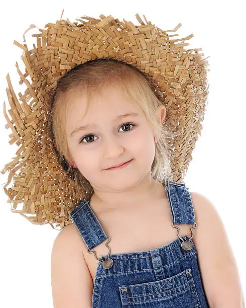 Head and shoulders image of an adorable preschool farm girl in overalls and a ragged straw hat.  On a white background.