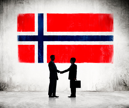 Two Businessmen Shaking Hands With Norwegian Flag As A Background