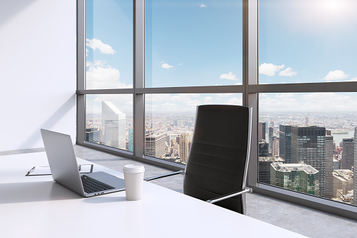 A workplace with laptop and a cap of coffee in a modern panoramic office, New York City view, Manhattan. A concept of financial consulting services. 3D rendering.