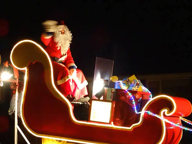 Photo showing a Santa Claus carnival float riding through the streets, with Father Christmas waving at the children.