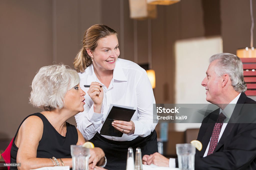 Waitress taking customer orders Waitress (30s) taking order from mature couple (50s) having business lunch.  Focus on waitress. 30-39 Years Stock Photo