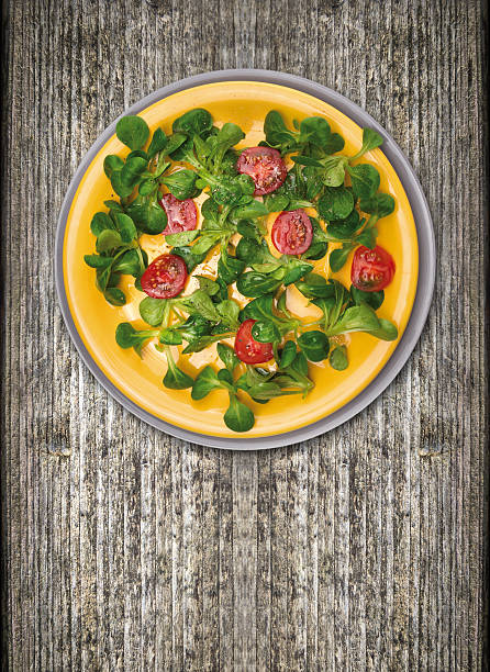 tomatoes with green salad, Serving in heavy yellow and gray plate on old wood