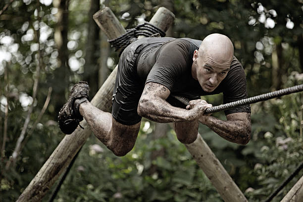 man climbing rope over mud obstacle man climbing rope over mud obstacle military camp stock pictures, royalty-free photos & images