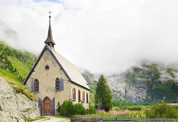 View from Gletsch in the Swiss Alps towards Furker Pass and the Rhone glacier. Gletsch's neo-Gothic Anglican chapel built in 1907-1908 can be seen in the foreground, and the Gletsch nature reserve, behind. The source of the Rhone can be seen in the background;  the Rhone glacier itself hidden behind the bare rock of the mountain side.
